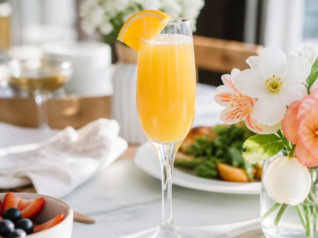 Mimosa i champagneglas med apelsinjuice och mousserande vin, garnerad med en apelsinskiva på ett soligt brunchbord