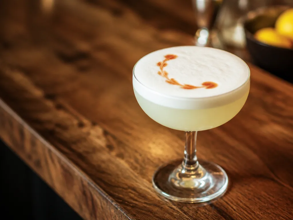 Pisco sour i ett lågt glas med tjockt vitt äggviteskum och droppar Angostura bitter på toppen