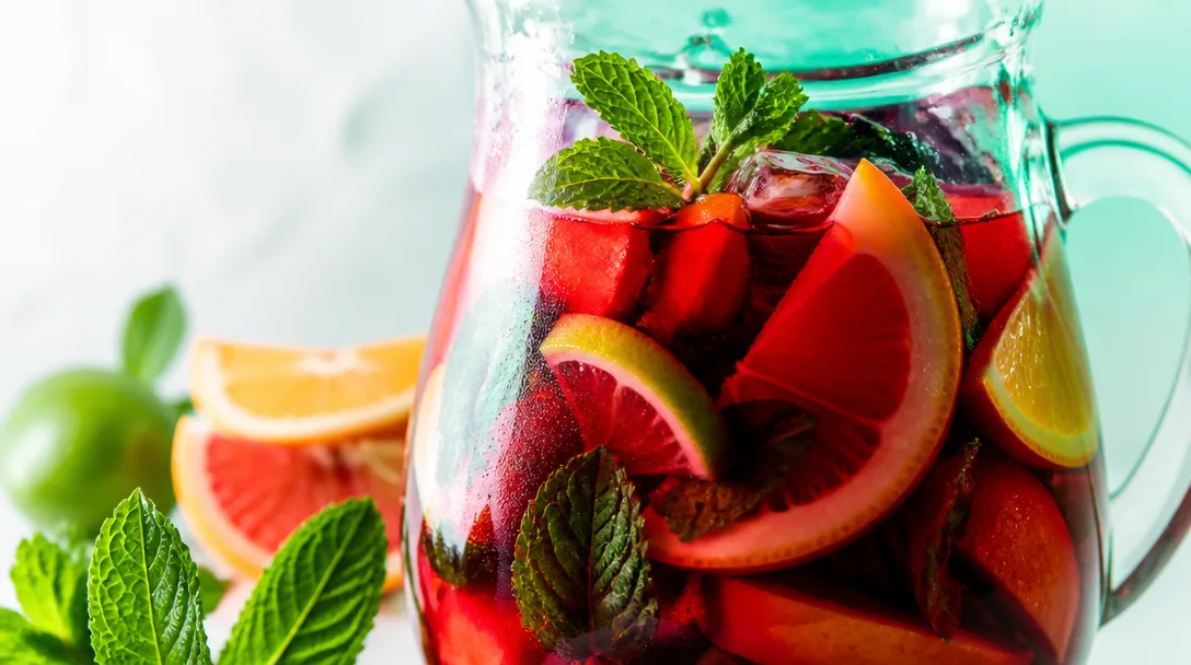 Vit sangria i karaff med persika, hallon och mynta
